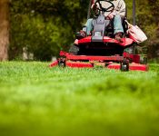 Gardener in the park on a lawn cutting tractor machine